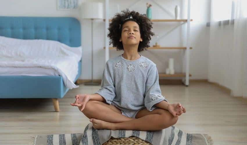 Black girl meditating in room with eyes closed